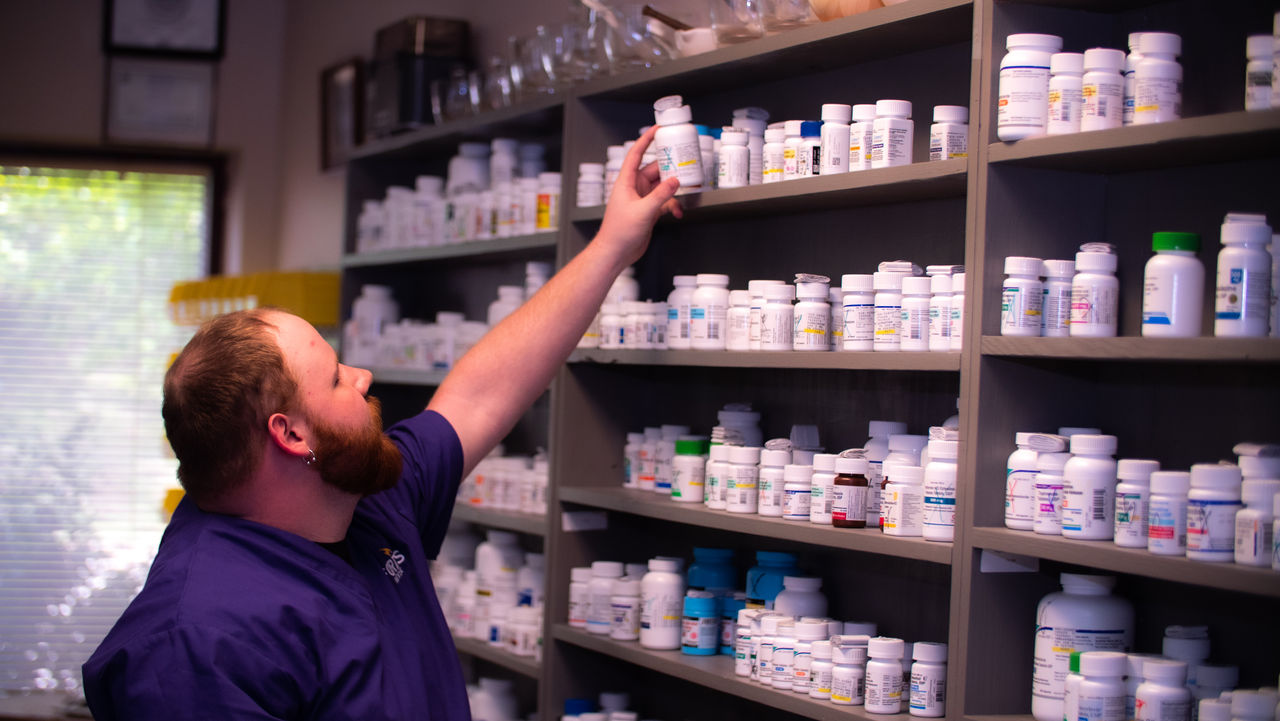 Pharmacy worker reaching for medication bottle on shelf